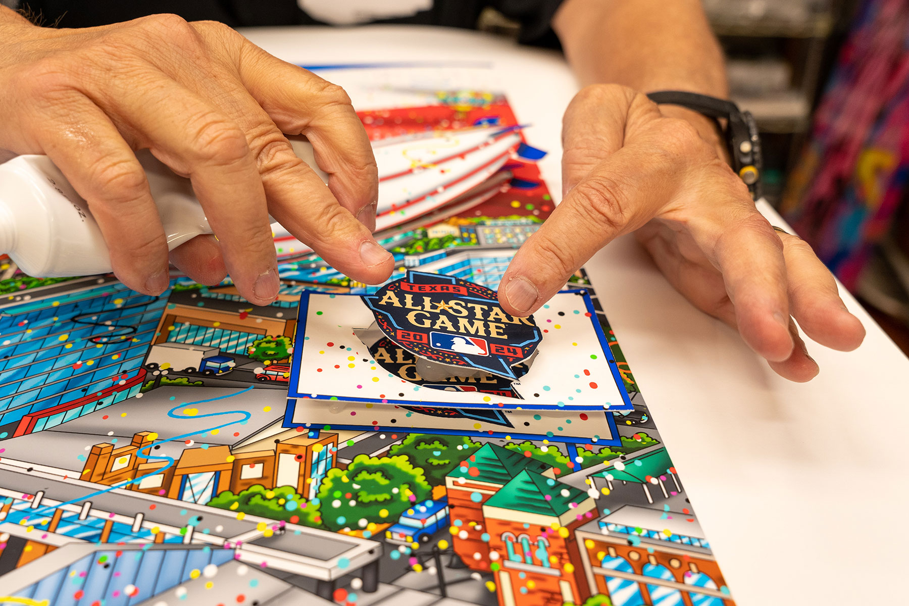 Fazzino's hands gluing down the MLB All-Star Game logo onto the limited edition 3D artwork to celebrate the event