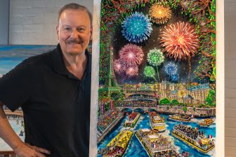 Fazzino stands next to his 2024 Paris Olympics artwork, the piece filled with boats in the Seine River and fireworks above the Eiffel Tower