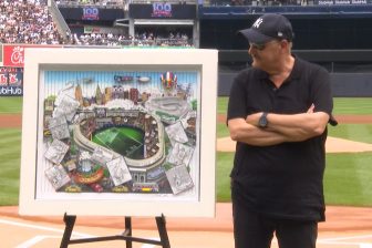 Fazzino standing in front of home plate at Yankee Stadium alongside his commemorative artwork for the 100 season mark for the NY Giants