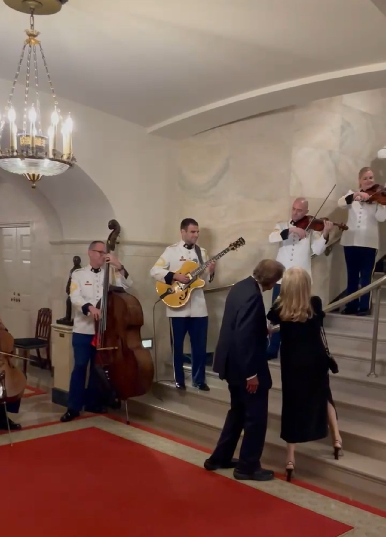 Joe Biden y el Dr. Biden suben las escaleras mientras un cuarto de cuerda se encuentra al costado de las escaleras tocando música.