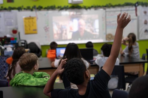 A student raises their hand to ask Fazzino a question while he talks to the students on a video call 