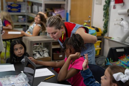 A teacher looks over the shoulder at a STEM student's work as she asks a question about the process