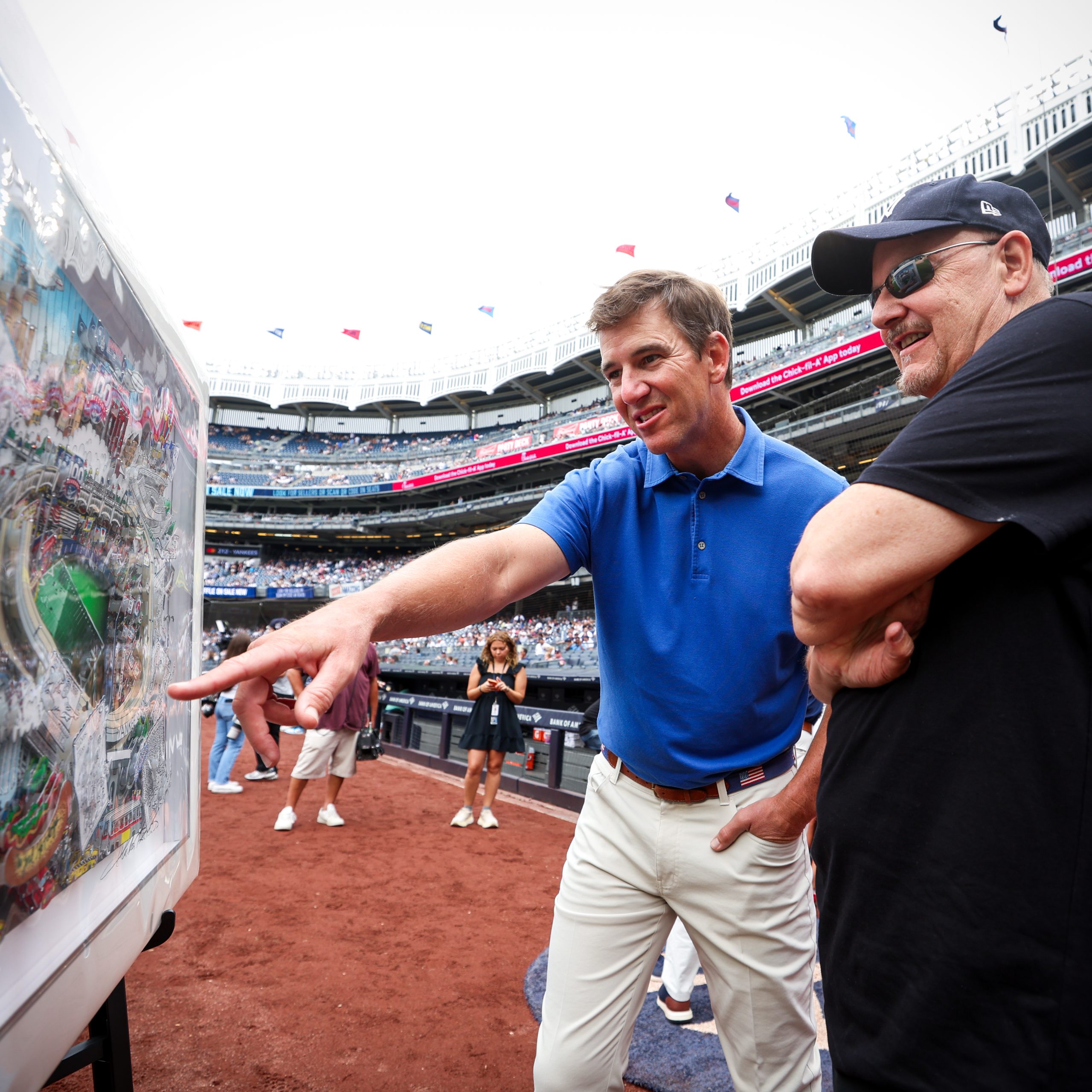 Fazzino stands with arms crossed while Eli Manning is next to him pointing at the artwork 